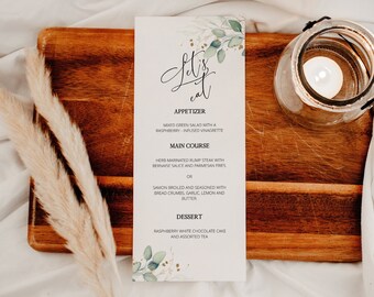 May include: A white menu card with the text "Let's eat" in black calligraphy. The menu lists appetizers, main courses, and desserts. The card is decorated with green watercolor leaves and gold glitter.