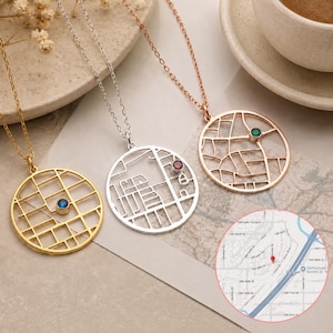 May include: Three circular pendant necklaces featuring a cutout street map design. One is gold with a blue stone, one is silver with a red stone, and one is rose gold with a green stone. A circular inset shows a digital map with a red location pin.