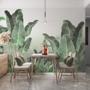 Puede incluir: Un comedor con una mesa de madera y dos sillas. Las sillas tienen cojines claros y cojines verdes. Un gran mural de hojas de plátano verdes adorna la pared. Una luz decorativa cuelga sobre la mesa y un jarrón con flores está sobre la mesa.
