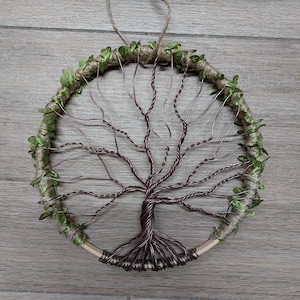 Könnte beinhalten: Ein Wandbehang aus Draht in Form eines Lebensbaums mit einem braunen Drahtrahmen und grünen Blättern. Der Baum ist mit Schnur umwickelt und hat einen rustikalen Look.