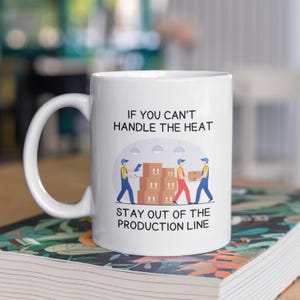 May include: White ceramic mug with a black and white graphic of three workers on a production line. The text on the mug reads "If you can't handle the heat stay out of the production line."
