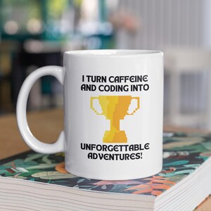 May include: White ceramic mug with a large handle. The mug features the text "I TURN CAFFEINE AND CODING INTO UNFORGETTABLE ADVENTURES!" and a pixelated gold trophy graphic. The mug is sitting on a book with a floral pattern.