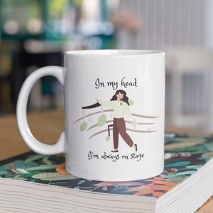 May include: White ceramic mug featuring a black and brown illustration of a person singing into a microphone with musical notes. The text "In my head I'm always on stage" is printed on the mug.
