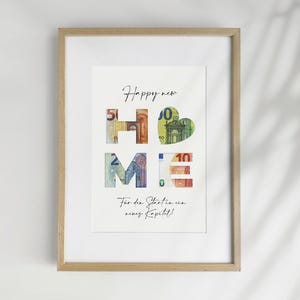 Könnte beinhalten: Gerahmter Kunstdruck mit dem Wort "HOME", das aus farbigen Euro-Banknoten gebildet wird. Die Worte "Happy new" stehen darüber und "Für den Start ins neue Kapitel!" darunter. Das Kunstwerk befindet sich in einem hellen Holzrahmen.