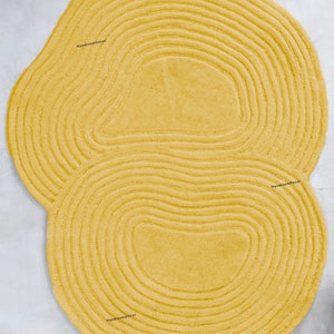 Könnte beinhalten: Ein runder, flauschiger Teppich in Gelb mit einer einzigartigen, organischen Form und konzentrischen Kreisen. Der Teppich hat eine weiche, plüschige Textur und ist perfekt, um jedem Raum einen Hauch von modernem Stil zu verleihen.