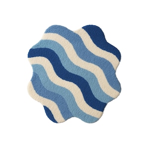 Könnte beinhalten: Ein einzigartig geformter Teppich mit einem wellenförmigen Muster in Blau- und Cremetönen. Der Teppich hat eine weiche, strukturierte Oberfläche und eine skurrile, wolkenartige Form. Das Design zeigt abwechselnde Streifen in Dunkelblau, Hellblau und Creme.