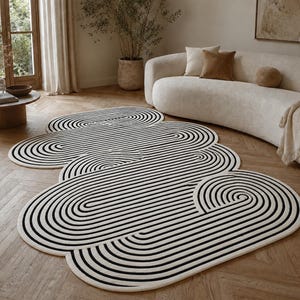 May include: A modern area rug with a unique design. The rug features a series of interconnected, oval shapes in black and white stripes. The rug is placed on a hardwood floor, and the room has a neutral color palette.
