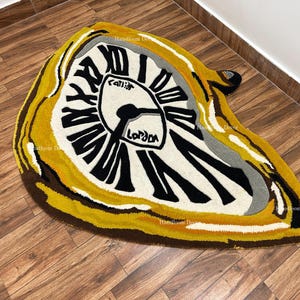 Może przedstawiać: Dywan w kolorze żółtym, brązowym i białym z wzorem roztopionego zegara. Tarcza zegara ma czarne cyfry rzymskie i napisy "London" i "Callie".