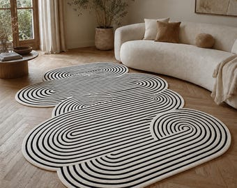 May include: An irregular, cloud-shaped area rug featuring a cream-colored base with a series of concentric black lines that follow the organic, rounded contours of the rug's perimeter, creating a repeating, layered, and swirling linear pattern.