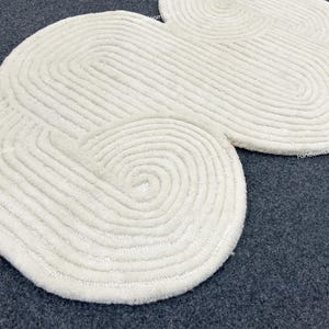 May include: A white cloud-shaped rug with a textured, woven design. The rug is made of soft, fluffy material and has a unique, modern look.