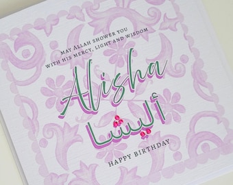 May include: A pink and white greeting card with a decorative border. The card says "May Allah shower you with his mercy, light and wisdom" and "Alisha" in green lettering. The Arabic word for Alisha is written in pink and green lettering. The card says "Happy Birthday" at the bottom.