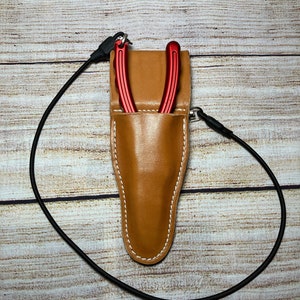 May include: A brown leather sheath with a red tool inside. The sheath has a white stitch detail and a black strap.