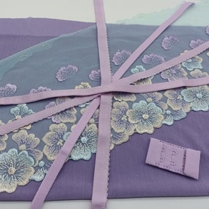Könnte beinhalten: Ein Set aus Lavendelstoff mit einer zarten floralen Spitzenborte und einem passenden BH-Verschluss. Der Stoff ist weich und durchscheinend, die Spitze ist filigran und wunderschön.