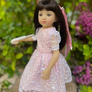 May include: A doll with long black hair wearing a pink lace dress and holding a pink and white umbrella.