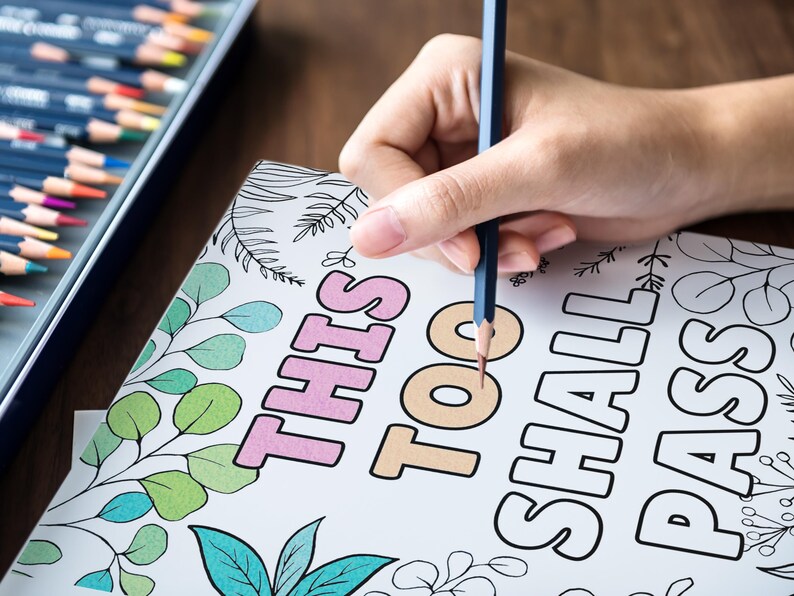 Puede incluir: Una p&aacute;gina para colorear con la frase "This Too Shall Pass" escrita en letras grandes y en negrita. La p&aacute;gina est&aacute; decorada con un patr&oacute;n de hojas y una mano sostiene un l&aacute;piz azul sobre la palabra "too".
