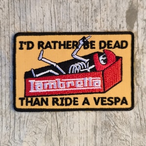 Peut inclure: Un écusson brodé jaune et noir avec un squelette dans un cercueil qui dit "I'd rather be dead than ride a Vespa" et "Lambretta" sur le cercueil.