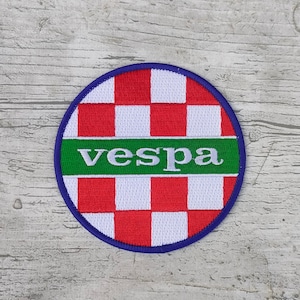 Puede incluir: Parche bordado redondo con un patrón de cuadros rojos y blancos, una franja verde con la palabra "vespa" en blanco y un borde azul. Para entusiastas de los scooters.