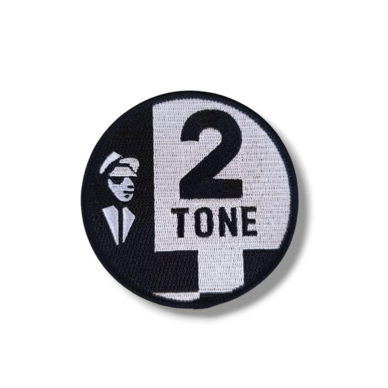 Puede incluir: Parche redondo en blanco y negro con el texto "2 TONE" y un dibujo de un hombre con gafas de sol. El n&uacute;mero 2 es una caracter&iacute;stica destacada. Este parche est&aacute; probablemente dise&ntilde;ado para su aplicaci&oacute;n en ropa o accesorios.
