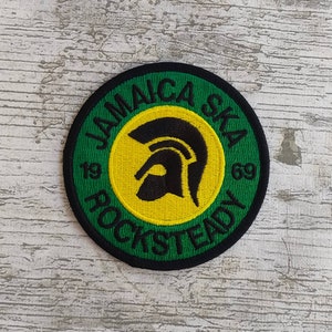 Op de afbeelding: Ronde patch met de tekst "JAMAICA SKA ROCKSTEADY 1969" in groene letters op een groene achtergrond. Het midden heeft een gele cirkel met een zwart helmsilhouet. De patch heeft een zwarte rand.