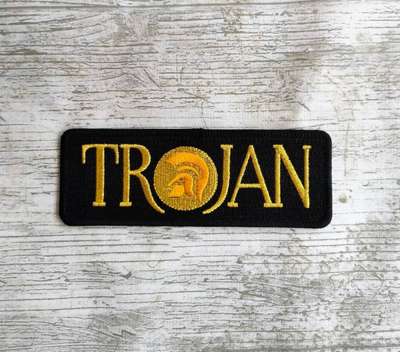 K&ouml;nnte beinhalten: Schwarzer gestickter Aufn&auml;her mit dem Wort "TROJAN" in goldenen Buchstaben und einer goldenen Helmgrafik.