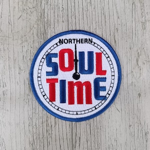 Può includere: Una toppa ricamata blu e bianca con il testo "NORTHERN SOUL TIME" in lettere rosse e blu. La toppa presenta un quadrante dell'orologio con una lancetta nera che punta alla parola "SOUL".