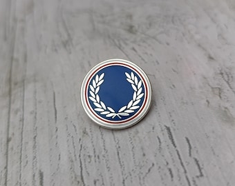 Broche de metal com coroa de louros da Fred Perry