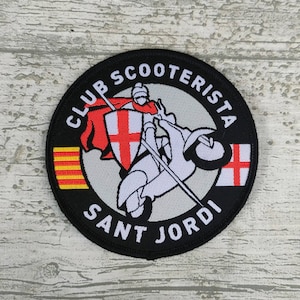 Puede incluir: Parche redondo negro con texto blanco "CLUB SCOOTERISTA SANT JORDI". Presenta un caballero en un scooter, una bandera roja y una cruz roja y blanca. También hay una bandera a rayas amarillas y rojas.