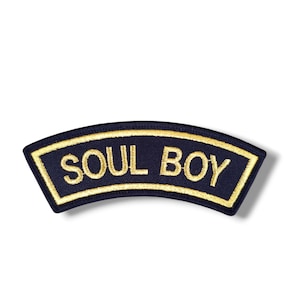 Puede incluir: Parche bordado azul marino con la inscripción dorada "SOUL BOY". El parche, de forma curvada, tiene un borde dorado. Diseñado para coser en ropa o accesorios.