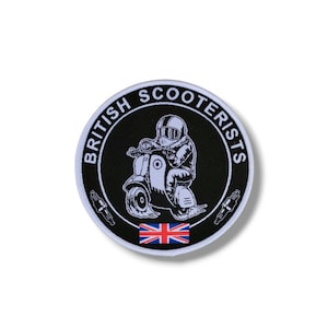 Może przedstawiać: Naszywka haftowana w kolorze czarnym i białym z tekstem "British Scooterists" w kółku wokół skutera z kierowcą w kasku. Flaga Unii Jacka znajduje się na dole naszywki.
