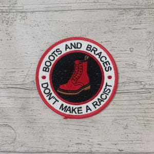 May include: Red and white embroidered patch with the text "Boots and Braces Don't Make a Racist" and a red boot with black laces.