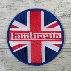 Peut inclure: Un patch rond brodé bleu, blanc et rouge avec le texte "Lambretta" en lettres blanches sur un fond blanc. Le patch présente un drapeau Union Jack stylisé.