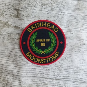 Op de afbeelding: Een zwarte en rode ronde patch met de tekst "SKINHEAD MOONSTOMP" in gele letters rond de rand. Het midden van de patch heeft een groene lauwerkrans met de tekst "SPIRIT OF 69" in gele letters.