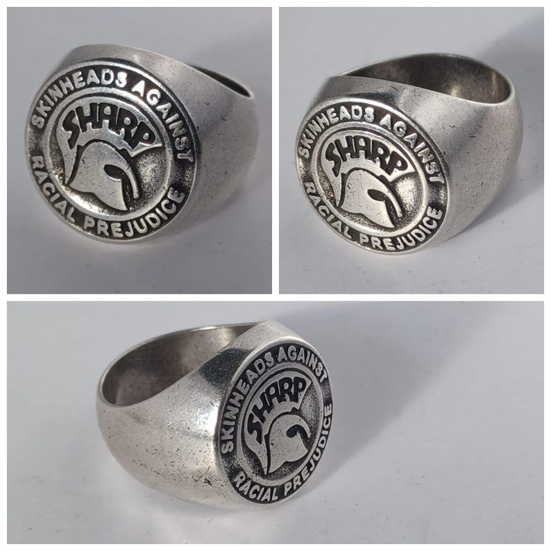 May include: A silver ring with a circular design featuring the text "Skinheads Against Racial Prejudice" and a stylized image of a Spartan helmet with the word "SHARP" above it.