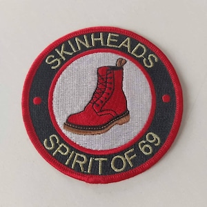 Könnte beinhalten: Runder, gestickter Aufnäher mit einem roten Stiefel in der Mitte. Die Worte "SKINHEADS" und "SPIRIT OF 69" sind in goldfarbenen Buchstaben geschrieben. Der Hintergrund ist weiß, mit einem schwarzen und roten Rand.