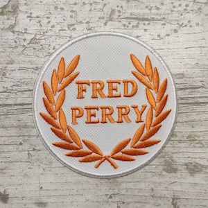 May include: White embroidered patch with an orange laurel wreath and the text "FRED PERRY" in the centre.