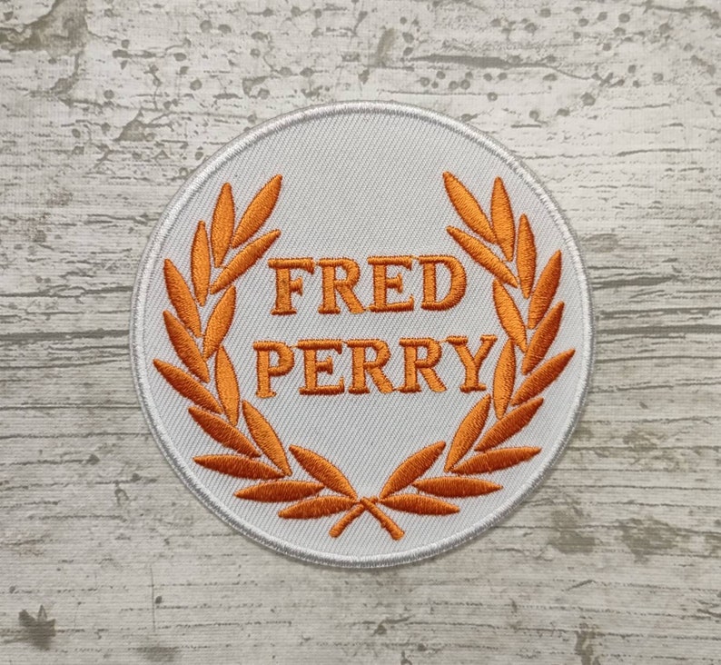May include: White embroidered patch with an orange laurel wreath and the text "FRED PERRY" in the centre.