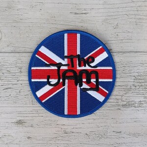 May include: A round embroidered patch with a Union Jack design and the text "The Jam" in black.
