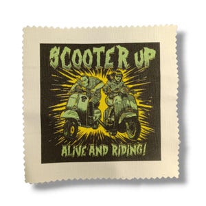 Puede incluir: Un parche cuadrado con fondo negro que muestra a dos personas montando en scooter, con las palabras "SCOOTER UP" y "ALIVE AND RIDING!" en verde y amarillo. El parche tiene un borde color crema con un borde en zigzag.