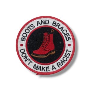 May include: Round embroidered patch with a red boot illustration inside a black circle. The patch has a white border with the words "BOOTS AND BRACES" and "DON'T MAKE A RACIST" in red text. The boot is red with brown soles.