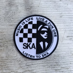 Puede incluir: Parche circular blanco y negro con el texto "Music is Life Live a Fun One Listen to Ska" y un patrón a cuadros y una silueta de una persona con gafas de sol y traje.