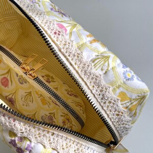 May include: A white quilted makeup bag with a floral print and a white lace trim. The bag is open and a smaller floral print zippered pouch is inside.