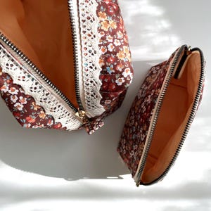 May include: Two floral print zippered makeup bags. The larger bag has a white lace trim. Both bags are open to show the beige lining.