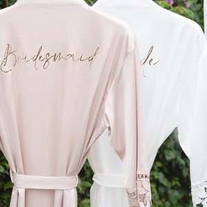 Pu&ograve; includere: Due accappatoi in raso con bordino in pizzo, uno in rosa cipria con la scritta "bridesmaid" in lettere dorate, e l'altro in bianco con la scritta "bride" in lettere dorate.