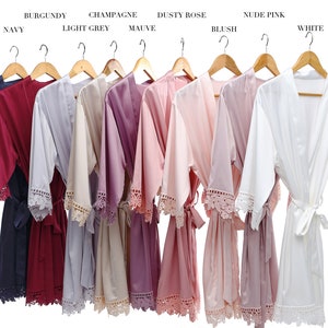May include: Ten satin robes in various colors, including navy, burgundy, light grey, champagne, mauve, dusty rose, blush, nude pink, and white. Each robe has lace trim and a tie belt.