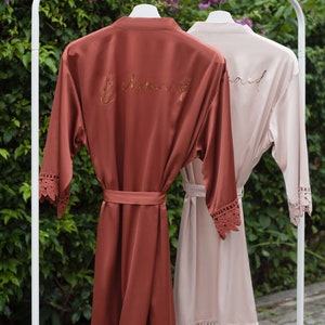 Pu&ograve; includere: Due accappatoi di raso con bordino in pizzo, uno color ruggine con "Bridemaid" ricamato in oro, l'altro color cipria con "Maid" ricamato in oro.