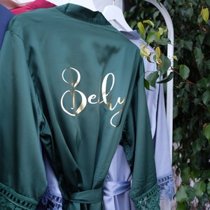 May include: A dark green satin robe with lace trim and the word "Bely" embroidered in gold on the back.