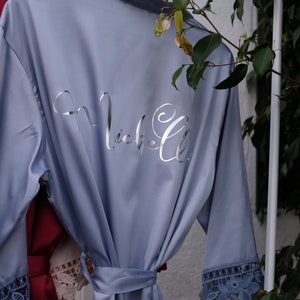 May include: A light blue satin robe with a silver embroidered name "Michelle" on the back. The robe has lace trim on the sleeves and a matching tie belt.