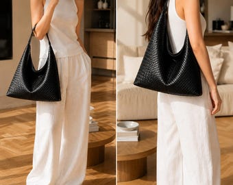 May include: A black hobo bag featuring a woven leather-like texture with a single shoulder strap. The bag has a slouchy, unstructured silhouette and a spacious main compartment, shown carried on the shoulder and held by the handle.