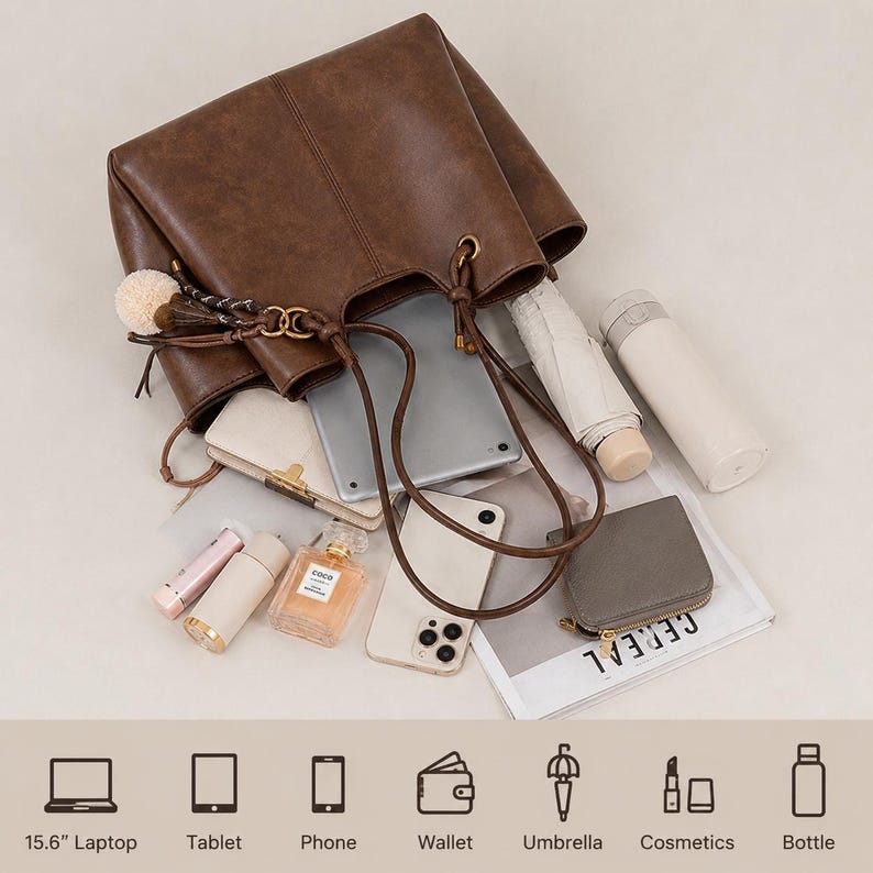 以下が含まれることがあります： ポンポンチャーム付きの茶色のレザータッチトートバッグ。中にはタブレット、スマートフォン、財布、折りたたみ傘、ボトル、化粧品が入っています。下部には15.6インチノートパソコン、タブレット、スマホ、財布、傘、化粧品、ボトルの収納容量を示すアイコンとテキストが記載されています。