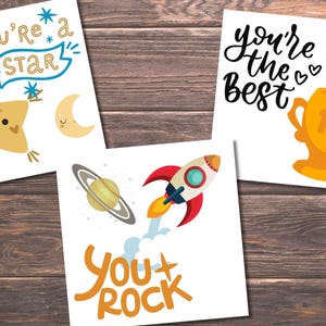Puede incluir: Tres tarjetas imprimibles con mensajes de &aacute;nimo. La primera tarjeta presenta una estrella amarilla con una cara sonriente y el texto "You're a star". La segunda tarjeta presenta un cohete y el texto "You rock". La tercera tarjeta presenta un trofeo dorado y el texto "You're the best".